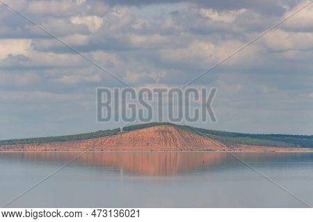 Lake With Clouds In The Sky, Red Hill With Forests On Background. Hill Symmetric Reflection In The W