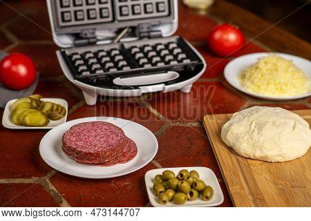Cooking Pizza Waffle, Piffle. Different Ingredients - Sausage, Olives, Pickles, Dough On The Kitchen