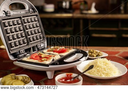 Cooking Pizza Waffle, Piffle. Waffle Iron And Different Ingredients On The Kitchen Table.