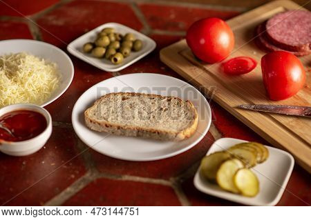 Sandwich Preparation. A Piece Of Bread On A Plate Surrounded By Various Ingredients.