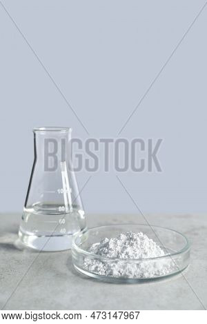 Petri Dish With Calcium Carbonate Powder And Laboratory Flask On Light Grey Table