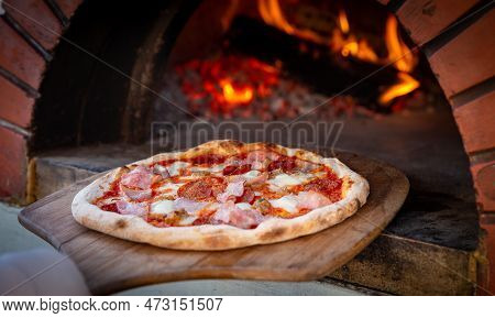 Chef Placing Pizza In Brick Oven To Be Cooked