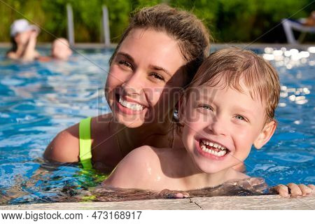 Happy Mothers With Young Son Swim In A Pool Of Warm Clear Water On Vacation. Satisfied Child Learns 
