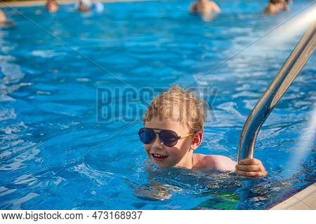 Satisfied Child Descends Into The Warm Pool In Fashionable Sunglasses, Hold The Metal Railing On The