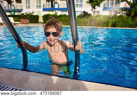 After Swimming In The Outdoor Pool, The Boy Climbs Out Of The Water Up The Steps, Holding On To Meta