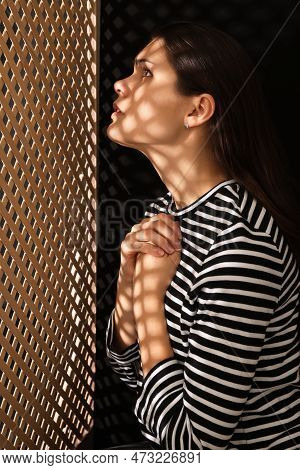 Woman Listening To Priest During Confession Near Wooden Partition In Booth