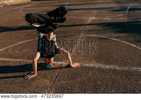 Teenage Boy Breakdancing On The Floor Of A Basketball Court. Caucasian Male Doing A Headstand. Youth