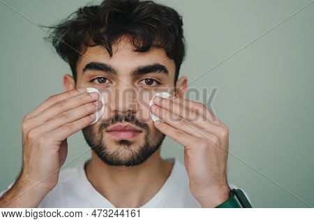 Front View Portrait Of A Handsome Man Cleaning Face Skin With Cotton Pads And Looking At Camera Over