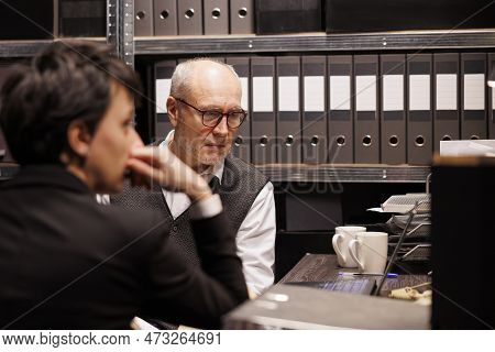 Elderly Police Officer Looking At Crime Scene Evidence On Laptop Computer, Discussing Criminal Case 