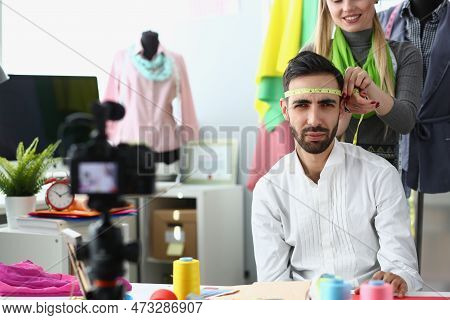 Woman Seamstress Stylist Jokes And Measures Head Of A Male Designer With Centimeter. Creative Worksh