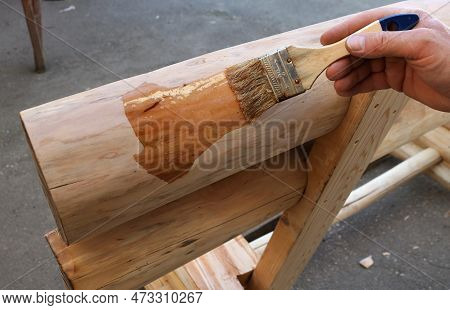 A Hand Applies A Layer Of Varnish With A Brush On A Fragment Of A Handmade Wooden Bench, Clear Varni