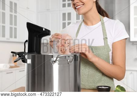 Woman Putting Vacuum Packed Meat Into Pot With Sous Vide Cooker In Kitchen, Closeup. Thermal Immersi