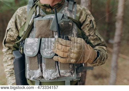 A Military Man In A Camouflage Uniform And Tactical Gloves Holds A Walkie-talkie. Communication Of T