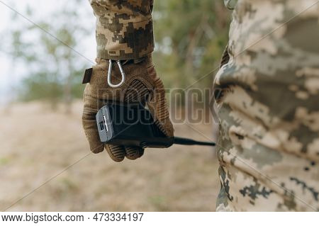 A Military Man In A Camouflage Uniform And Tactical Gloves Holds A Walkie-talkie.