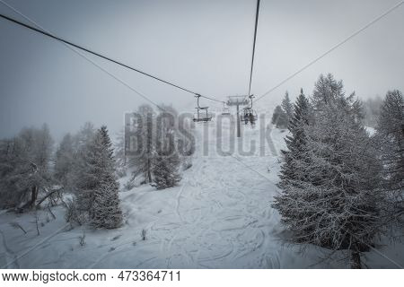 Ski Lift Transports Skiers And Snowboarders In Foggy Day At Snowy Mountain. Frozen Funicular. Pinzol
