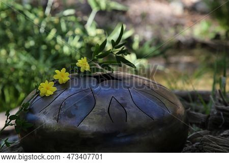 Steel Tongue Drum And Yellow Flowers Outdoors. Percussion Musical Instrument