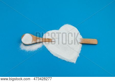 White Powder Is Scattered On Blue Surface In Shape Of Heart. Wooden Spoon With Collagen Or Protein. 