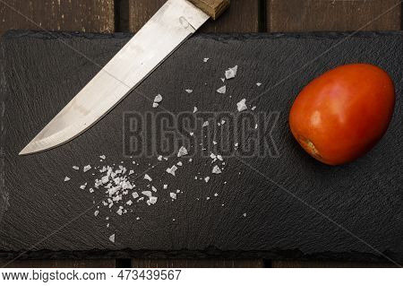 A Ripe Cherry Stupendous Tomato On A Black Slate Along With Salt Flakes And A Wooden Handled Kitchen