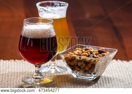Glasses Of Belgian Yellow Blond And Dark Brown Beer Made In Abbey Served In Bar With Party Nuts