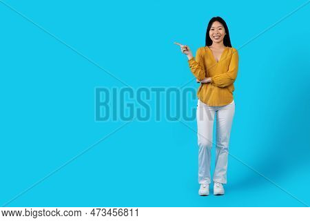 Cheery Young Asiam Lady Pointing At Copy Space On Blue