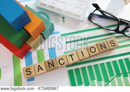 Word Sanctions With Wooden Blocks On Paper Diagrams In Office Upper View. Ban Of International Busin