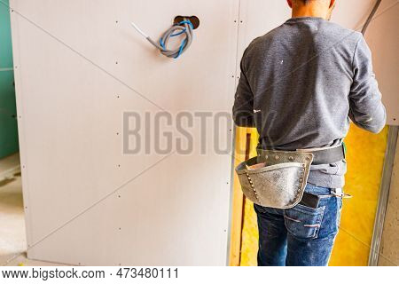 Shot From Behind Of Worker With Tool Bag Around His Waist, Works On The Installation Of Plasterboard