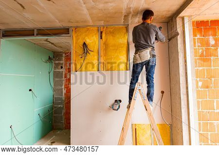 Repairman On Wooden Ladder Holds Professional Manual Power Tool Acu Drill And Tightens The Screws On