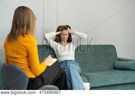 Young Woman At A Psychologist's Appointment Is Sitting On The Couch And Holding Her Head, Experienci