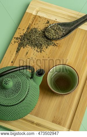 Top View Image Of Traditional Green Tea Set And Black Porcelain Spoon With Dry Tea On Brown Bamboo T