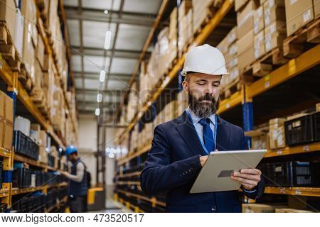 Manager In Suit Controlling Goods In A Waehouse.