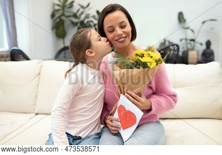 Happy Caucasian Small Daughter Kisses On Cheek, Congratulates Young Mother On Women Day, Birthday