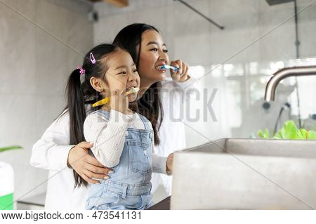 Asian Little Girl With Mom Brushing Teeth In Bathroom, Korean Woman Helping To Brush Daughter's Teet