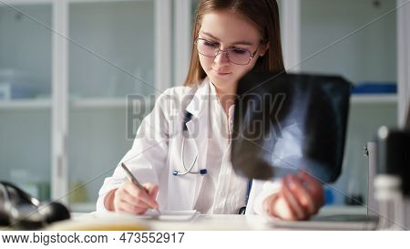 Therapist Doctor Holding Xray Of Lungs In Hands And Writing In Medical Documents In Clinic. Diagnosi