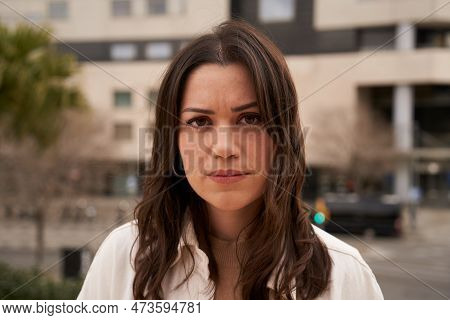Serious Young Caucasian Girl Looking At Camera Outdoors. Close Up Of Worried Earnest Woman.