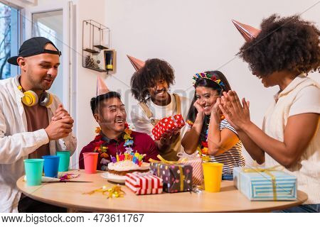Multi-ethnic Group Of Friends At A Birthday Party On The Sofa At Home With A Cake And Gifts, Smiling