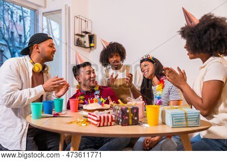 Multi-ethnic Group Of Friends At A Birthday Party On The Sofa At Home With A Cake And Gifts, Smiling