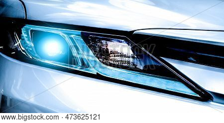 Closeup Headlamp Light Of A White Luxury Car. Automotive Industry Concept. Electric Car Or Hybrid Ve