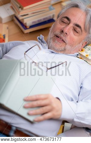 Peaceful And Positive Man With Dreamy Expression Sleeping Among Numerous Books Resting On The Floor.