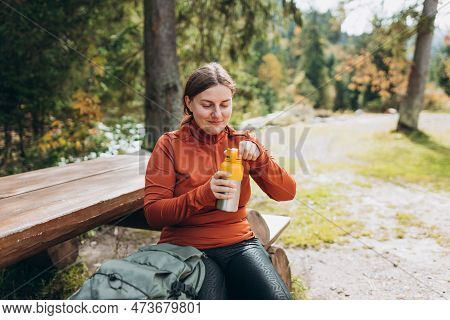 Happy Redhead Woman In Active Trekking Clothes Having A Halt After Hiking. Hiker Drinking Water From