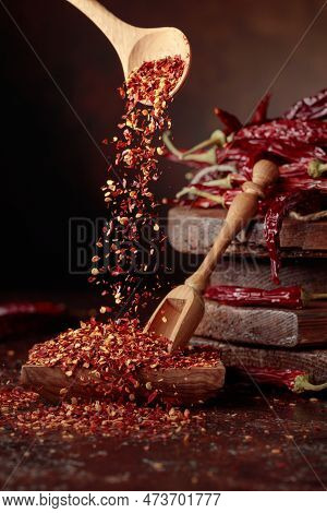 Chilli Flakes Are Poured Into A Wooden Dish. Chilli Flakes And Dried Chili Peppers On A Brown Backgr