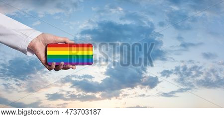 Hand Holding Smartphone With Lgbt Glag On The Background Of Blue Cloudy Sky. Support, Stop Discrimin