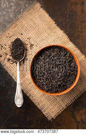 Dry Black Tea Leaves In A Clay Bowl And A Vintage Spoon On A Dark Background Top View. Large-leaf An