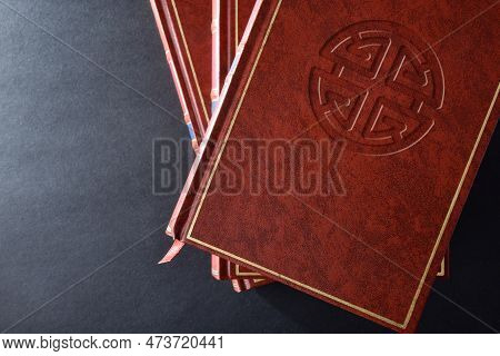 Stack Of Books With Brown Leather Cover With Engraved Symbol Of Shenist Culture And Religion On Blac