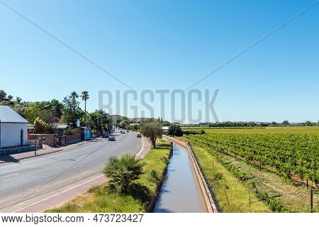 Keimoes, South Africa - Feb 25, 2023: A Street Scene, With Irrigation Canal And Vineyards, In Keimoe