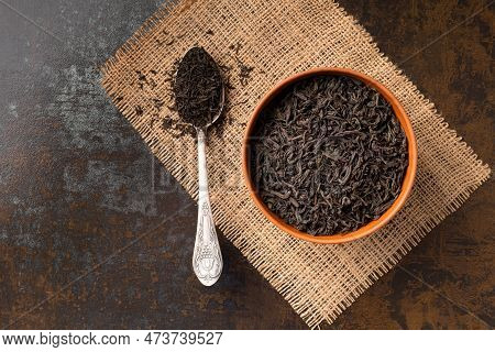 Dry Black Tea Leaves In A Clay Bowl And A Vintage Spoon On A Dark Background Top View. Large-leaf An