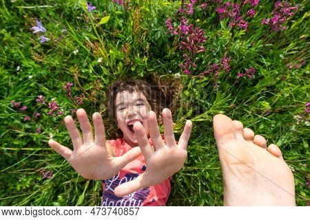 Portrait Of A Child Girl In Summer Lying In The Grass And Wildflowers With Heels And Palms. Summer T