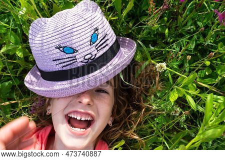 Portrait Of A Child In A Hat With His Face Covered In Summer Lying In The Grass And Wildflowers. Hat