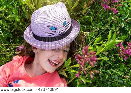 Portrait Of A Child In A Hat With His Face Covered In Summer Lying In The Grass And Wildflowers. Hat