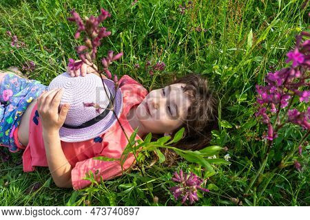 Portrait Of A Child In A Hat With His Face Covered In Summer Lying In The Grass And Wildflowers. Hat