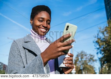 From Below Optimistic African American Female In Stylish Outerwear With Zero Waste Cup Of Coffee Smi